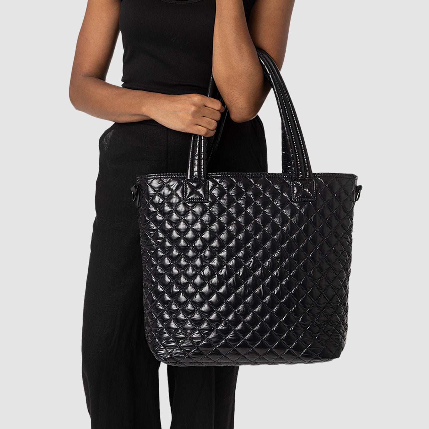 Woman holding a large, black quilted handbag.