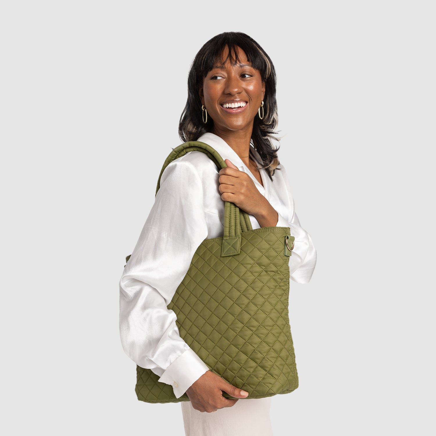 A person smiling and holding a green quilted tote bag.