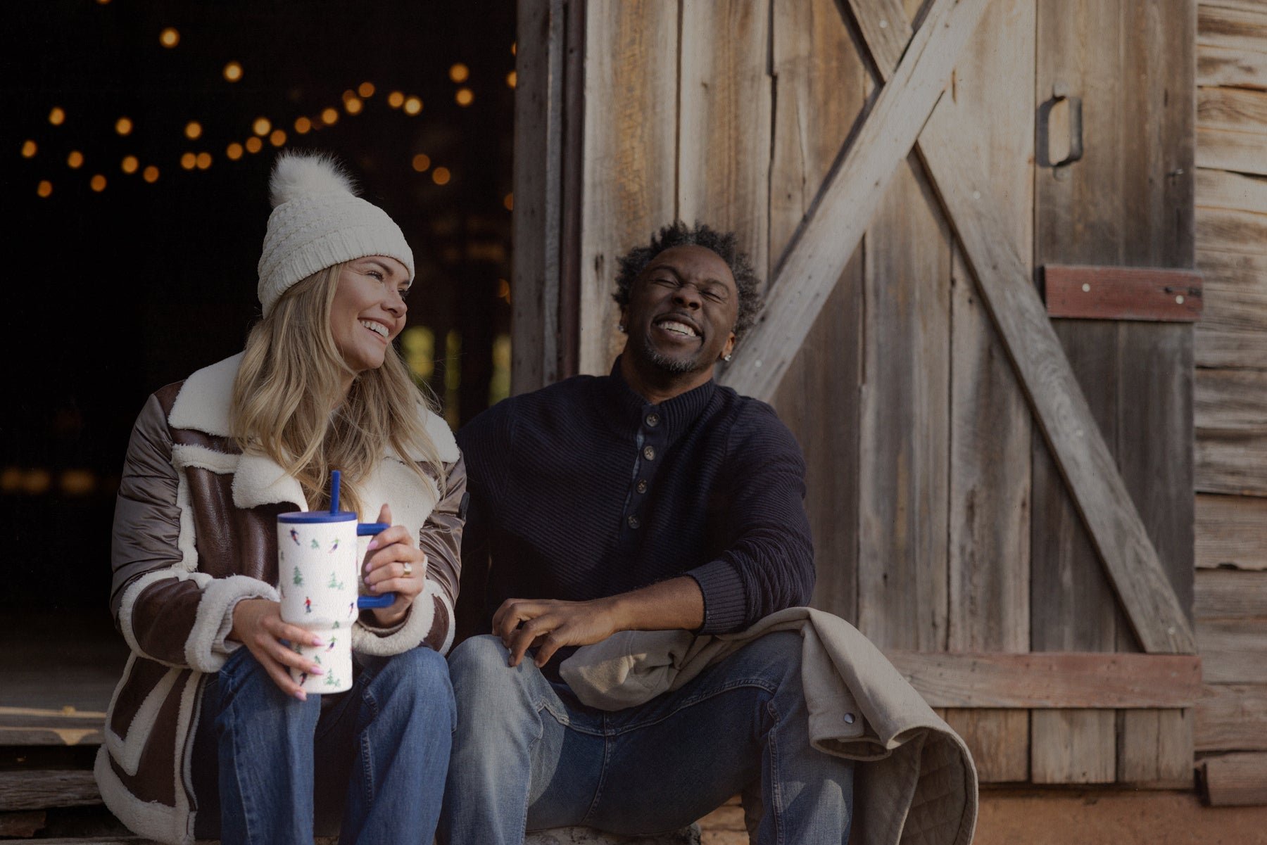 Two people sitting and laughing outside a rustic wooden building.